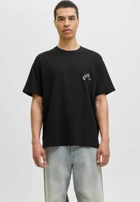 Sort bomulds t-shirt med korte ærmer, afslappet pasform og et broderet logo på brystet. Sammen med lette, falmede denimjeans.