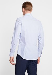 Modrá a bílá pruhovaná košile s dlouhými rukávy, špičatým límcem, zakřiveným dolním lemem a zapínáním na knoflíky na rukávech. Bavlněná tkanina s jemnou strukturou.