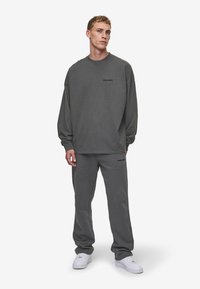 Gray sweatshirt with long sleeves and a round neck, paired with matching tapered sweatpants, both featuring subtle branding in black.