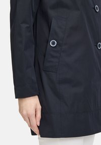 Marineblauer wasserdichter Jacke mit geknöpften Taschen, glattem Textur, geradem Schnitt und kontrastierenden Steppdetails.