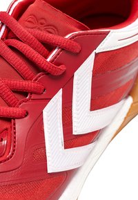 Baskets de sport rouges avec un empeigne texturée, des accents blancs et un motif en zigzag prononcé. Les lacets sont rouges avec une finition en tissu.