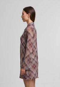 Rochie transparentă, cu carouri în tonuri estompate de mov, bej și albastru. Prezintă un guler, mâneci lungi și un tiv ondulat. Material ușor, cu o croială lejeră.