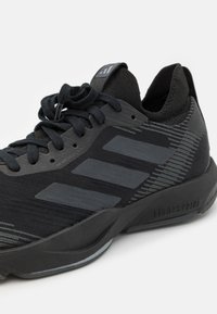 Sneaker atletica nera con tre strisce grigio scuro, tomaia in maglia, colletto imbottito e suola spessa e ammortizzata su uno sfondo bianco.