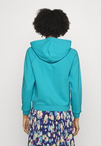 Teal hoodie med dragsko i huven, ribbade ärmar och nederkant samt en avslappnad passform, kombinerad med en blommig plisserad kjol.