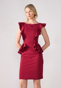 Rød tettsittende kjole med volanger på skuldrene og peplum midje. Laget av glatt stoff, knelength med rund hals.