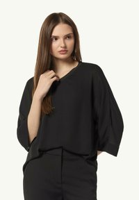 Black loose-fitting blouse with a V-neckline and dropped sleeves, made of smooth fabric, paired with black pants. No notable patterns or accents.