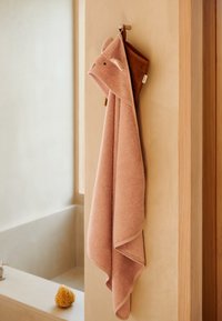 Różowy ręcznik z kapturem z uszami misia, wykonany z miękkiego materiału, zawieszony na ścianie. Posiada zaokrąglone uszy i wyszywane detale twarzy.
