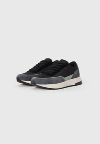 Atletische sneakers met een mix van zwart en grijs suède en stof, een ronde neus, platte veters en een dikke witte tussenzool met een gestructureerde rubberen buitenzool.