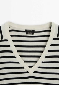 Sweter w paski wykonany z bawełny, z dekoltem w serek. Posiada naprzemienne czarne i kremowe paski. Metka wskazuje, że wykonany jest w 100% z bawełny.