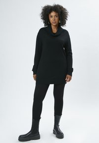 Túnica negra de punto con cuello de cisne, mangas largas, lados texturizados y dobladillo acanalado, combinada con leggings negros y botas negras gruesas.