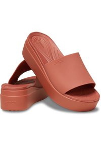 Sandalias de goma corales con una correa ancha, plantilla acolchada y suela de plataforma gruesa. Presentan una superficie suave con un fondo texturizado.