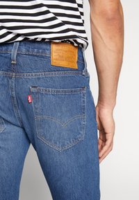 Blå denimjeans med en läderlapp märkt "Levi Strauss & Co." på midjan och karakteristisk bakficka med V-formad sömnad.