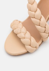 Sandale beige avec deux larges brides tressées sur le pied et un design à bout ouvert lisse.