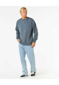 Grauer Baumwollpullover mit Rundhalsausschnitt, lockerer Passform, gerippten Säumen, kombiniert mit hellblauen Jeans und schwarzen Sneakers.