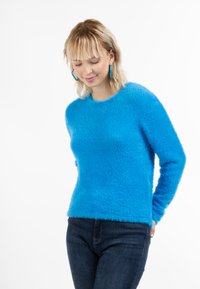 Maglione blu soffice con scollo rotondo e maniche lunghe, abbinato a jeans di denim scuro. Texture morbida, colore vivace e vestibilità casual.
