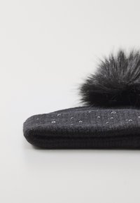Chapeau en laine noir avec un pompon en fourrure douce, présentant un motif de tricot texturé et de petites perles décoratives à l'avant.