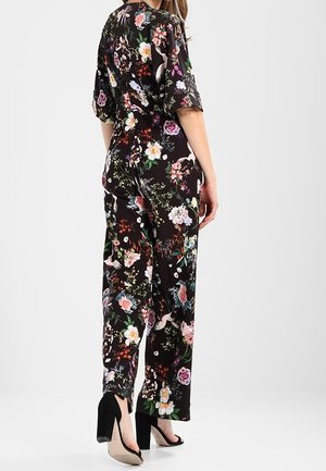 Czarny kombinezon w kwiaty z krótkimi rękawami, z kolorowymi kwiatami i ptakami. Ma luźny krój i jest zestawiony z czarnymi szpilkami.