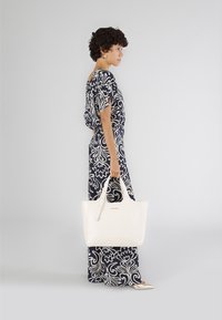 Witte leren tas met stevige handvatten, met een minimalistisch ontwerp en subtiele stikdetails. Achtergrond is lichtgrijs.