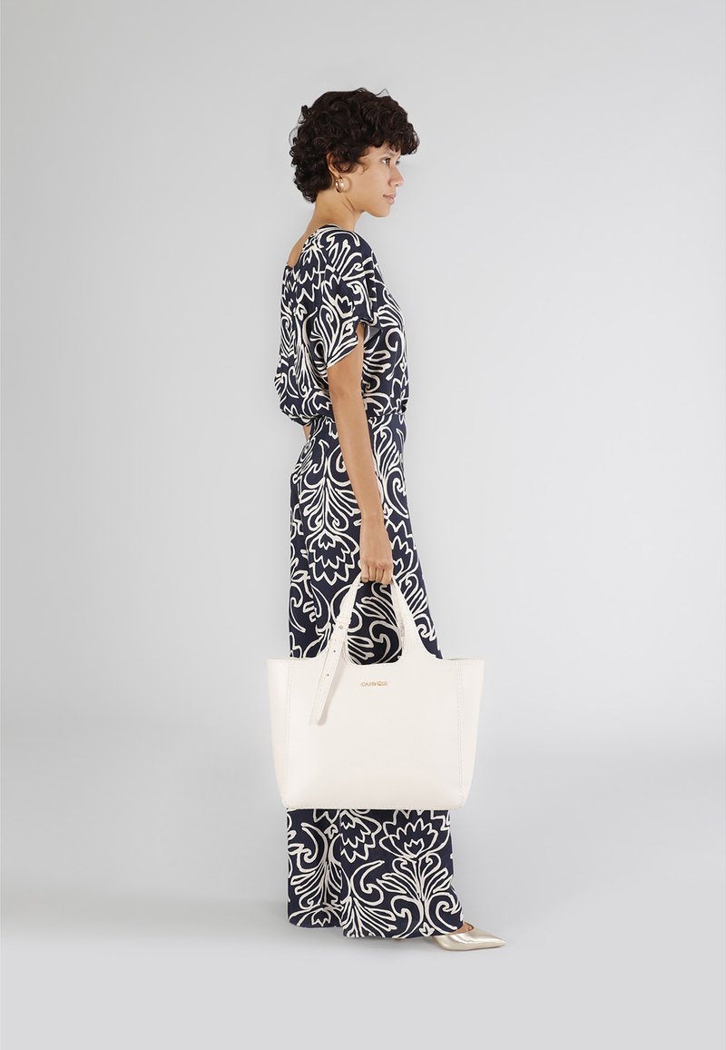 Borsa tote in pelle bianca con manici robusti, caratterizzata da un design minimalista e dettagli di cucitura sottili. Sfondo grigio chiaro.