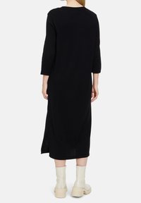Robe midi noire avec manches trois-quarts, fentes latérales et coupe décontractée. Portée avec des bottines crème pour contraste. Texture lisse.