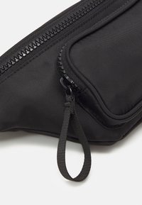 Sacchetto nero realizzato in tessuto testurizzato con chiusura a zip. Presenta un piccolo gancio e una tasca laterale, evidenziando un design elegante.