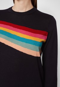 Pull noir à manches longues avec des rayures diagonales rouges, roses, jaunes, bleues, vertes et beiges sur la poitrine, porté par une personne.