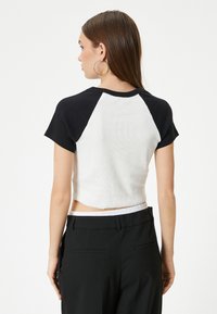 Korte T-shirt met zwarte korte mouwen en een witte geribbelde romp, met een ronde hals en een licht gebogen zoom. Gepaard met zwarte broeken.