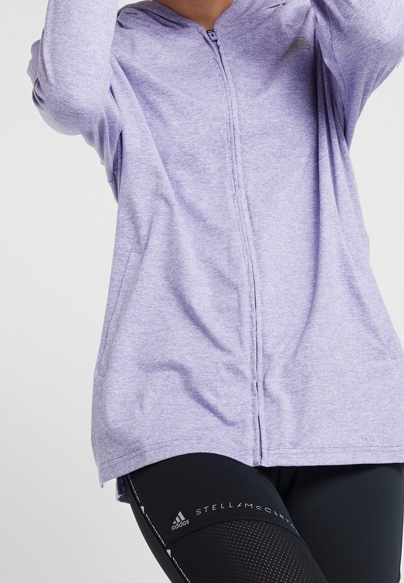 Felpa a zip di colore viola chiaro con cappuccio, maniche lunghe e tasche laterali. Presenta un tessuto liscio e texture e un design aderente.
