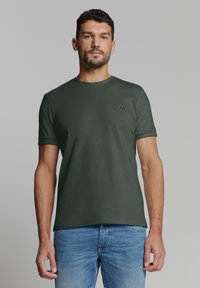 Donkergroene T-shirt met korte mouwen van katoen, voorzien van een ronde hals en een klein hexagonaal logo op de linkerborst. Aansluitend ontwerp.