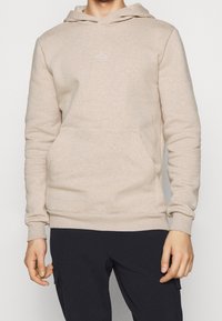 Sudadera beige hecha de una tela suave, con un bolsillo canguro y un logo blanco de perchero en el pecho, con puños y dobladillo de canalé.
