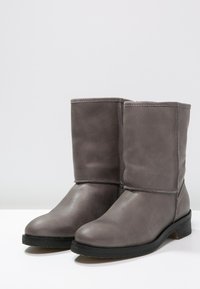 Šedé kožené kotníkové boty s kulatou špičkou, plochou podrážkou a minimálním prošíváním. Hladký povrch s jemným leskem.