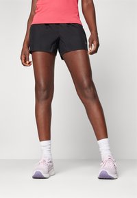 Pantalones cortos deportivos negros de corte relajado, material ligero y con el logo de ASICS. Combinados con zapatillas rosas y calcetas blancas.