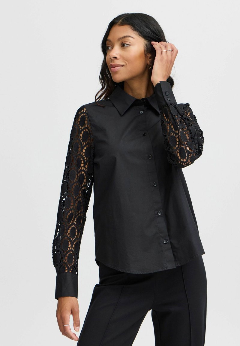 Schwarze Hemdbluse mit einfarbigem Front und kunstvollen Spitzentrikots mit kreisförmigen Mustern, taillierter Kragen und taillierte Manschetten.
