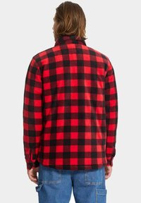 Camisa de franela a cuadros rojos y negros, con cuello alto, mangas largas y textura suave. Vista completa desde atrás con dobladillo redondeado.