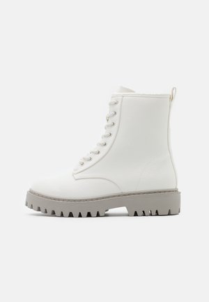 Vita snörkängor av syntetiskt material, med en tjock grå gummisula med djupa spår och en dragflik bak.