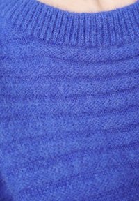 Blauer gestrickter Pullover mit einem gerippten Halsausschnitt, weicher Textur und subtilem horizontalem Muster. Fokus auf Wärme und lässiges Design.