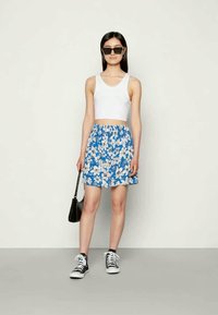 Saia azul estampada com flores, acompanhada de uma blusa curta branca. Ténis pretos e uma pequena mala preta completam o visual.