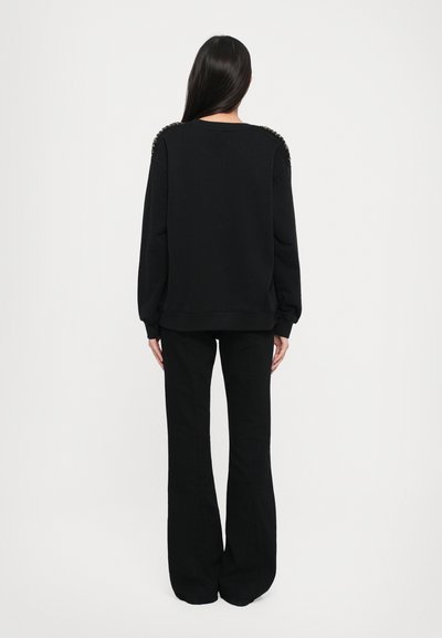 Czarna bluza z haftami na ramionach, luźny krój, długie rękawy, w połączeniu z czarnymi spodniami w kształcie dzwonów, widok z tyłu.