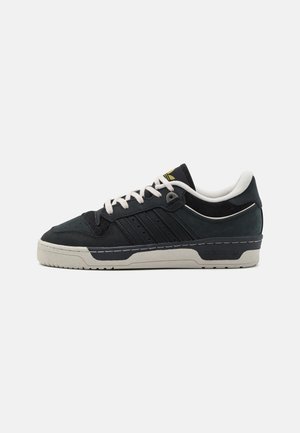 Czarne zamszowe sneakersy z białą gumową podeszwą, beżowymi akcentami i trzema bocznymi paskami. Posiadają sznurowanie oraz perforowane detale na czubku.