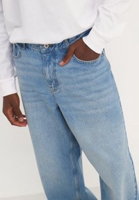 Ljusblå denimjeans med avslappnad passform, fem fickor och subtila blekningar. Har en metallknapp och en enda bältesöggla.