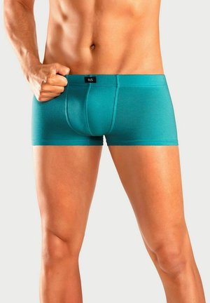 Fit torso and legs wearing teal boxer briefs, with one hand gripping the waistband against a plain light background.