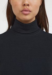 Sort ribbet turtleneck med en tætsiddende pasform og en struktureret stof. Den høje krave og den glatte overflade fremhæver plaggets struktur.