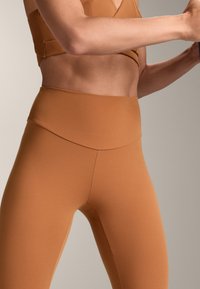 Visoko pasirani, prilegajoči leggingi v mat rjavi barvi, ki imajo brezšivni pas in gladko, raztegljivo tkanino.