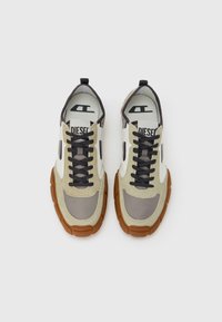 Bež in sive superge z masivnim gumijastim podplatom. Vključujejo mešanico tekstur, črne vezalke in izstopajoč logotip na vložku.