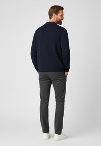 Granatowy sweter robiony na drutach z fakturowanym wzorem, zestawiony z szarymi spodniami slim-fit i białymi trampkami, widoczny z tyłu.