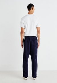 Mørkeblå joggebukser med hvite sidestriper, elastisk midje og baklomme; kombinert med en enkel hvit t-skjorte.