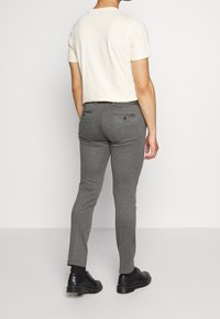 Grå slim-fit byxor med en slät yta, med två bakfickor och en standardmidja, kombinerat med en ljus krämfärgad t-shirt.