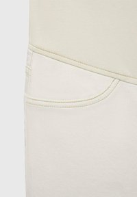 Ljust beige topp med sömlös design, parat med vita denimbyxor med en enda framficka och subtila sömnadsdetaljer.