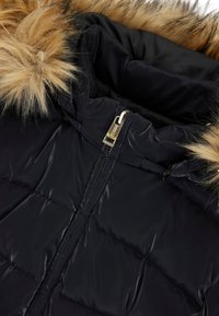 Giubbotto di piuma nero con cappuccio in pelliccia sintetica, dotato di una texture lucida, chiusura a zip e design trapuntato. Accent del hardware in oro sulla zip.