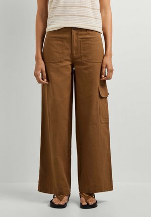 Pantaloni marroni a gamba larga con tasche applicate davanti e ai lati, indossati con sandali e top a righe senza maniche.